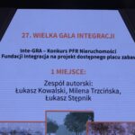Wyświetlony na sześciokątnym ekranie kadr, informujący, że laureatem pierwszego miejsca w konkursie na projekt dostępnego placu zabaw został Zespół autorski w składzie: Łukasz Kowalski, Milena Trzcińska oraz Łukasz Stępnik