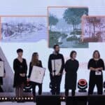 Siedem osób stojących na scenie, od lewej wszyscy wyróżnieni oraz laureaci konkursu na projekt dostępnego placu zabaw „Inte-GRA”, a także Pani Zuzanna Mielczarek (architekt, specjalistka ds. projektów społecznych i innowacyjnych w PFR Nieruchomości) oraz Pan Adam Włodzimierz Wach (architekt, audytor dostępności w Fundacji Integracja)