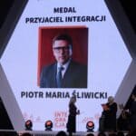Stojące na scenie trzy osoby, od lewej: Pani Monika Truszkowska-Bednarek – Prezes Fundacji Integralia, Pani Ewa Pawłowska oraz Pan Tomasz Wolny; za nimi widać sześciokątny ekran z wyświetlonym portretem Pana Piotra Maria Śliwickiego wyróżnionego Medalem „Przyjaciel Integracji”; widok z widowni