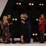 Pięć osób na scenie, od lewej muzyczne małżeństwo Paulina i Bartek Gruszeccy, Pani Ewa Pawłowska w serdecznym uścisku z Panem Tomaszem Wolnym oraz kobieta w czerwonej sukience, trzymająca bukiet kwiatów