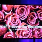Ekran z białym napisem „Dzień Pracownika Socjalnego, 21 listopada 2022 r. umieszczonym na tle róż w kolorze różowym.