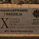 Metalowa tabliczka umieszczona na pamiątkowej statuetce, zawiera logo Caritas Diecezji Siedleckiej oraz napis drukowanymi literami: „niepełnoSPRAWNI i nadzieja / IX Festiwal Filmowy Twórczości Osób Niepełnosprawnych / WTZ Biała Podlaska 2022”