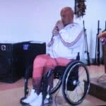 Kadr z filmu „Nadzieja”, zrealizowanego przez DPS w Kozuli, przedstawiający śpiewającego do mikrofonu Pana Grzegorza Przybysza - siedzącego na wózku inwalidzkim łysego mężczyznę w średnim wieku, ubranego w strój sportowy (dres)