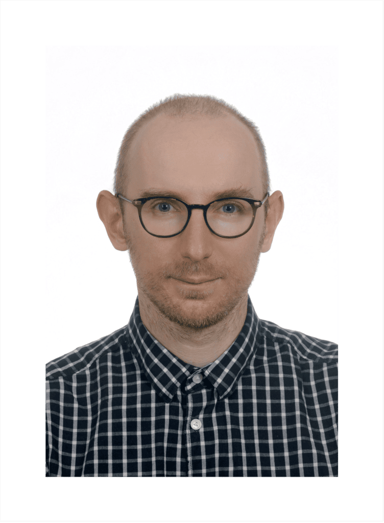 Portret zdjęciowy młodego mężczyzny z brodą i w okularach.