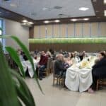 Siedzące przy zastawionych stołach rodziny z dziećmi uczestniczące w Projekcie „Rodzinne Wędrówki”