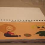 Stronica z książki autorstwa Pani Katarzyny Michailidis pt. “Hania i Mania”, przedstawiająca ilustrację dotykową z napisem “Dziewczynki grają w piłkę”