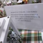 Biała kartka wielkości A4 z czarnym napisem „Warsztat Terapii Zajęciowej Polskiego Stowarzyszenia na Rzecz Osób z Niepełnosprawnością Intelektualną Koło w Tarnobrzegu”, umieszczona pomiędzy świątecznymi dekoracjami rękodzielniczymi, przeznaczonymi do sprzedaży podczas Mikołajkowego Jarmarku Pracy