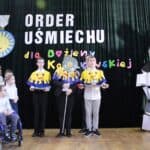 Członkowie Kapituły Orderu Uśmiechu oraz Marek Michalak (Kanclerz Kapituły Orderu Uśmiechu) stojący wśród uczniów SOSW dla Dzieci i Młodzieży Niepełnosprawnych im. Prof. Zofii Sękowskiej w Lublinie