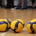 Sześć zółto-niebieskich piłek leżących na parkiecie boiska