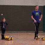 Mała dziewczynka, stojąca przy trzech piłkach w towarzystwie, stojącego przy dwóch piłkach w podobnej pozycji - Artura Bożyka - trenera AZS UMCS,