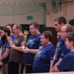 12 zawodników stojących w rzędzie z pucharem