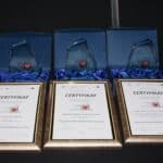Trzy certyfikaty oprawione w złote ramy, w tle trzy szklane statuetki z logo zakup pro społeczny.