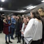 Grupa młodych osób oglądająca zdjęcia na wernisażu wystawy fotograficznej "Pokazać światu siłę. Kadra narodowa Ukrainy w judo osób niesłyszących"