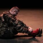 Na scenie siedzi aktor w przebraniu, odgrywający tytułową rolę kota w spektaklu pt. „Kot w butach”; zakłada na nogi czerwone sznurowane buty