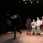 Scena w spektaklu pt. "Kot w butach": na scenie stoi tytułowy "kot w butach" w towarzystwie trzech zamaskowanych postaci, przed którymi tańczy ubrany na czarno Czarodziej w przerażającej masce