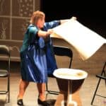 Scena ze spektaklu pt. „W kawiarni Zegarynka”: kelnerka nakrywa kawiarniany stolik białą serwetą