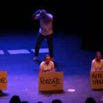 Scena ze spektaklu pt. „Różni-Równi”: trzy siedzące aktorki trzymają w rękach duże tekturki, na których napisano słowa, układające się w zdanie: "SĄ RÓŻNE RODZAJE NIEPEŁNOSPRAWNOŚCI"