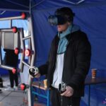Stoisko Lubelskiej Akademii WSEI: młody mężczyzna korzysta z gogli wirtualnej rzeczywistości, po jego prawej stronie stoi symulator refleksu Simflex