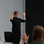 Nauka podstawowych zwrotów Polskiego Języka Migowego przez Panią Jolantę Gromadę - gest uniesionych w górę rąk, poruszanych na boki w nadgarstkach, oznaczający "brawa"