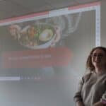 Pani Ewelina stojąca przy ścianie, na której prezentowany jest slajd pt. "Wzory żywieniowe a sen"