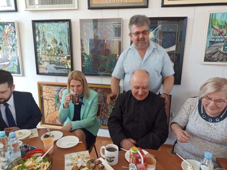 Pan Jarosław Chabros w towarzystwie siedzących przy stole Gości zaproszonych na Spotkanie Wielkanocne Stowarzyszenia "Otwarty Krąg"