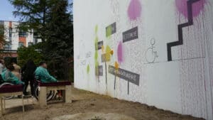 Uczestnik happeningu na wózku, rzucający balonik wypełniony farbą w "szary" mural