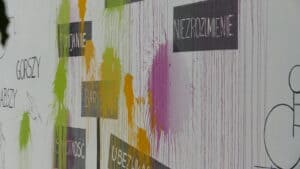 "Szary" mural z hasłami dyskryminacji, pokrytymi kolorowymi plamami z farb