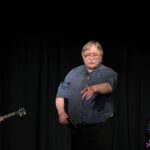 Pan Marek Kowal wskazujący ręką na osobę z widowni, która wygrała płytę CD