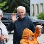 Dwoje seniorów i osoba na wózku; mężczyzna macha do kamery