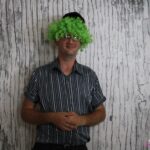 Uczestnik w zielonej peruce pozuje do zdjęcia w fotobudce