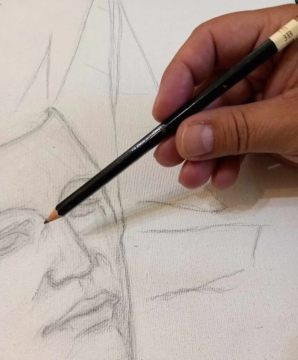 Dłoń trzymająca ołówek poprawia zarys nosa ukończonego szkicu twarzy mężczyzny