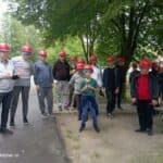 Grupa osób w kaskach stoi na tle drzew