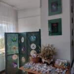 Na zielonym parawanie wiszą hafty wykonane metodą tradycyjną, na stole leżą zakładki i breloki wykonane haftem diamentowym, a w koszach w płócienne torebki spakowano zioła z opisem