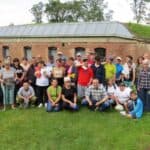 Zdjęcie uczestników przy budowli obronnej ceglanego budynku z oknami zabezpieczonymi metalowymi tablicami