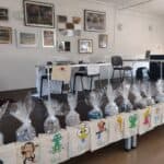 Wystawa prac wszystkich uczestników projektu: koszyczki zapakowane w foliowe torebki, torebki ręcznie malowane i haftowane, w tle obrazy zdrapywane