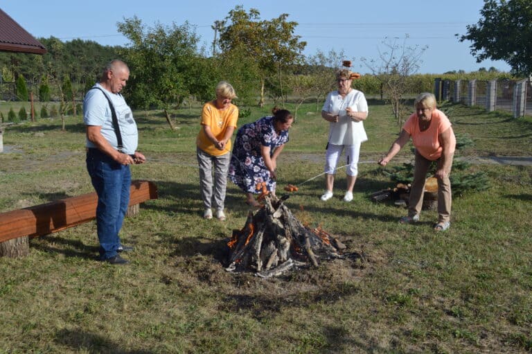 Cztery kobiety i mężczyzna pieką kiełbaski nad ogniskiem