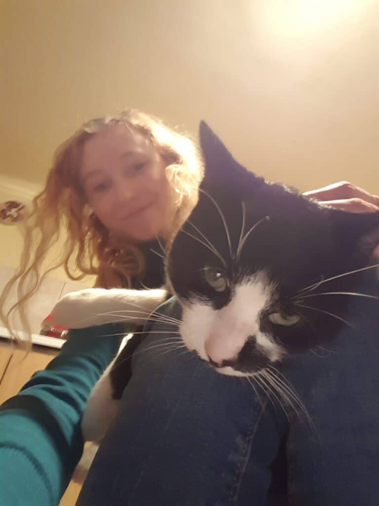 Magdalena, długowłosa usmiechnięta blondynka trzyma na kolanach biało-czarnego kota