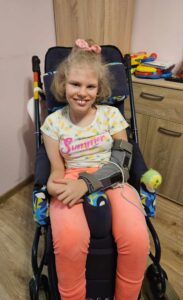 Lenka siedzi na wózku, na lewej ręce ma stabilizator.