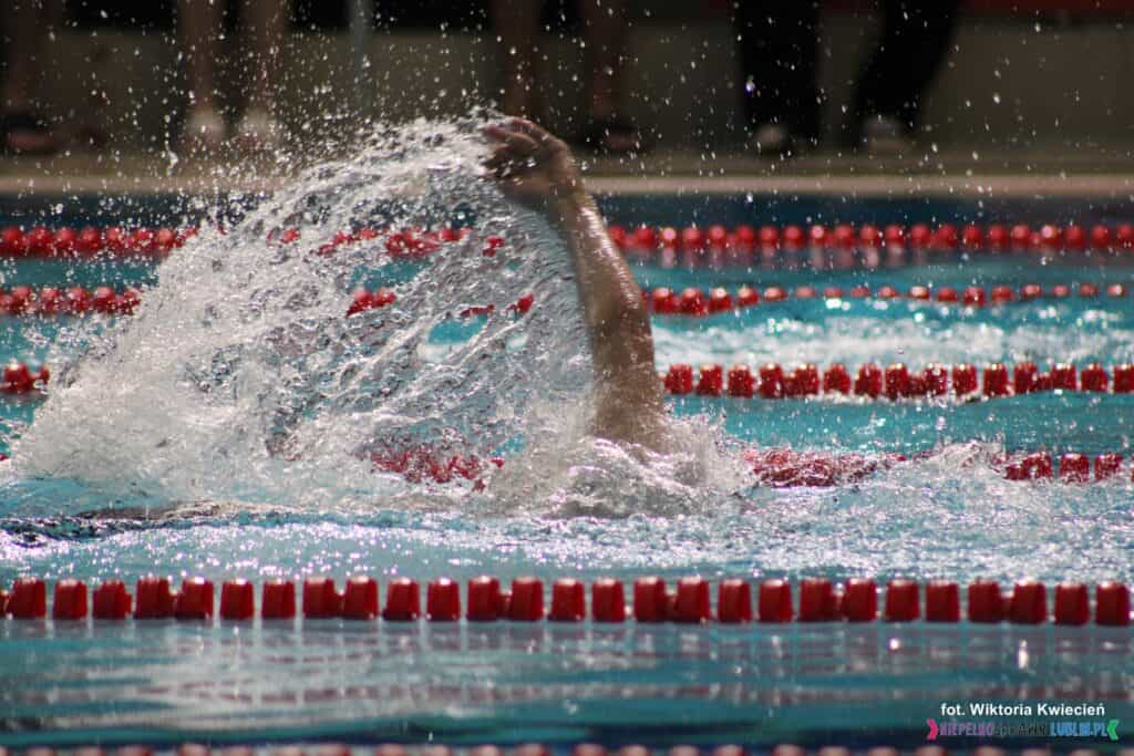 Ponad taflą basenu uniesiona ręka pływaka rozbryzguje wodę