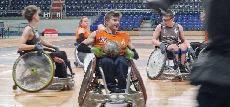 Dominik na specjalnym "pancernym" wózku do gry w rugby na wózkach w trakcie meczu - trzyma piłkę w rękach w specjalnych rękawicach