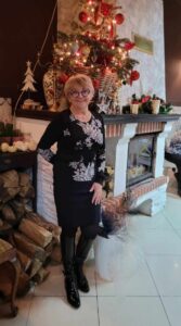 Barbara Zielonko - kobieta z krótkimi blond wlosami w czarnych okualrach, usmiechnięta, ubrana na czarno - krotka spódnica i bluzka z białą aplikacją w kwiaty.