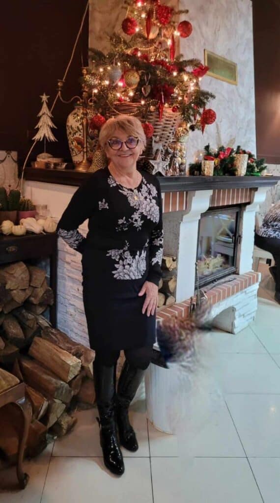 Barbara Zielonko - kobieta z krótkimi blond wlosami w czarnych okualrach, usmiechnięta, ubrana na czarno - krotka spódnica i bluzka z białą aplikacją w kwiaty.