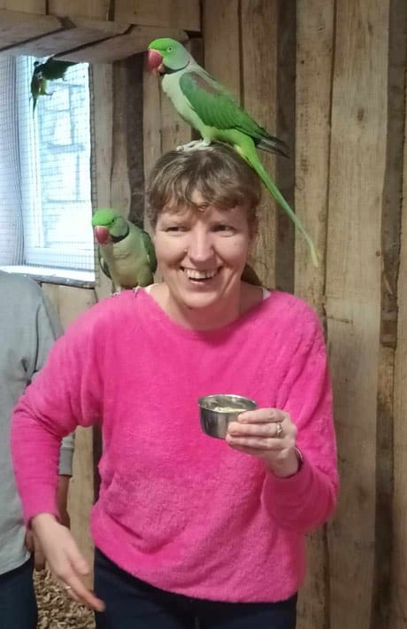 , na jej ramieniu i głowie siedzą duże zielone papugi.