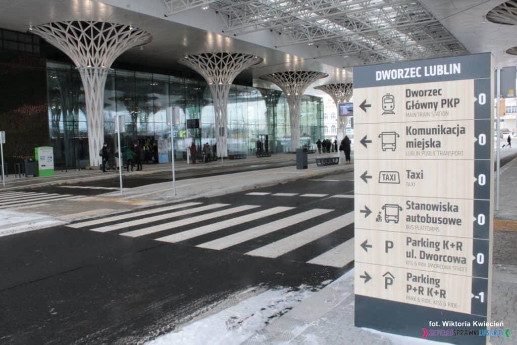 Tablica informacyjna, w tle wejście do budynku dworca