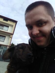 Tomasz Dziubak - uśmiechnięty młody człowiek z ciemnymi krótko ostrzyżony włosami z psem Lusią