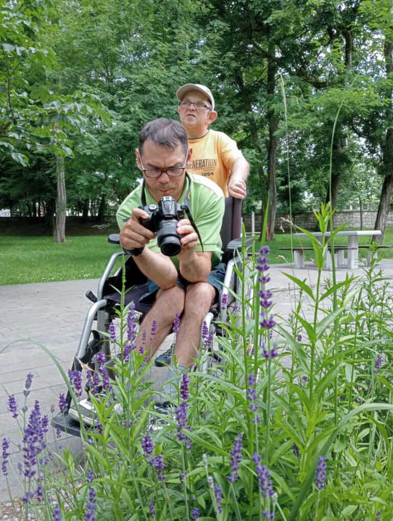 Krzysztof Warzocha siedząc na wózku fotografuje krzak lawendy