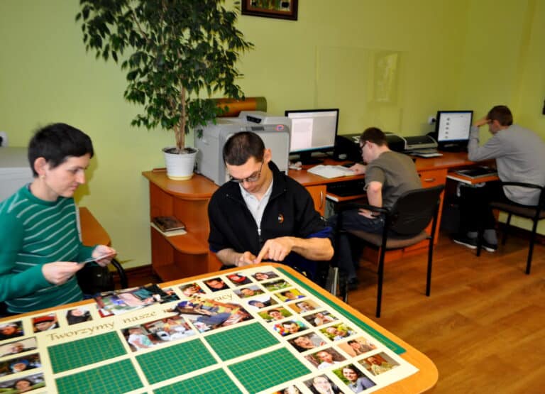 Krzysztof w trakcie pracy w pracowni poligraficznej w WTAZ - Siedzi przy stole i przygotowuje plansze ze zdjęciami