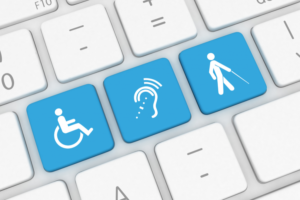 Klawiatura komputera, na której trzy klawisze zostały zastąpione ikonami symbolizującymi dostępność. Pierwszy klawisz przedstawia osobę na wózku inwalidzkim. Drugi klawisz ma ikonę ucha z promieniującymi liniami. Trzeci klawisz pokazuje postać idącą z pomocą laski. Pozostałe klawisze są białe i mają standardowe symbole klawiatury oraz litery.
