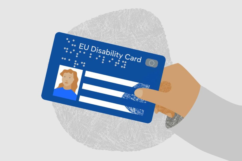 Karta z napisem: EU Disability Card, trzymana w dłoni. Karta jest niebieska, z białym i jaśniejszym niebieskim tekstem, oraz z alfabetem Braille'a