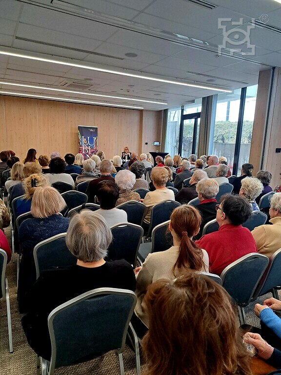 Seniorzy zgromadzeni w sali konferencyjnej Hotelu Arche, słuchający wykładu.